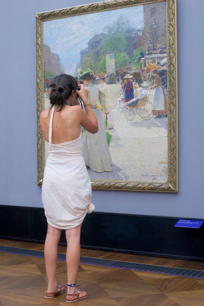 Девушка в белом сарафане фотографирует картину